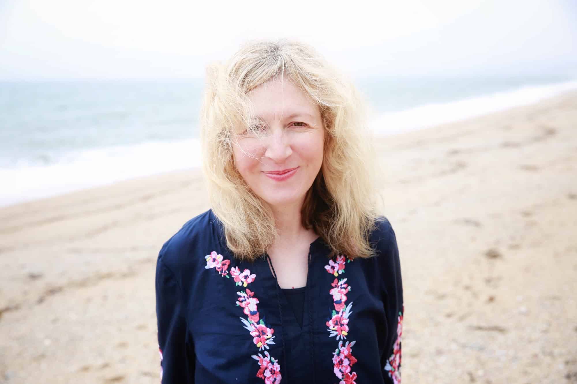 A happy and smiling 40 year old woman on a sandy beach in a wellbeing concept portrait